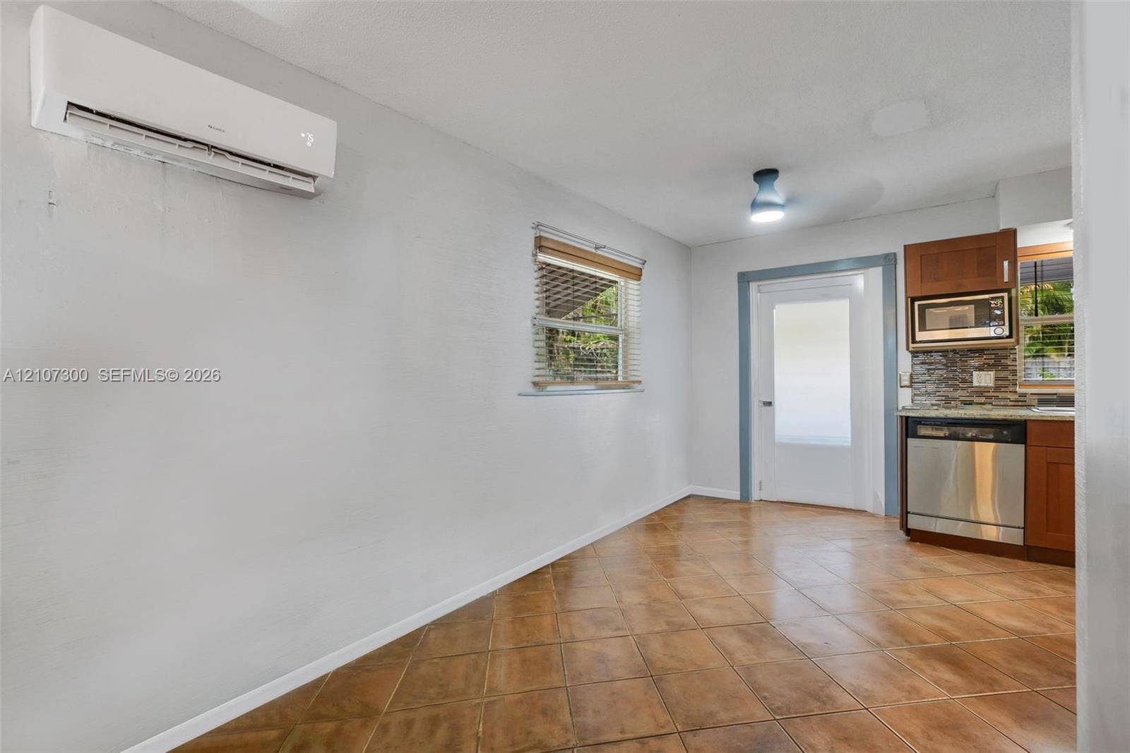 2051 NE 68th Street, Fort Lauderdale, FL 33308 Wall-mounted ductless air conditioning unit, tile flooring, window with blinds, full-lite exterior door, and built-in kitchen cabinetry with stainless steel appliance