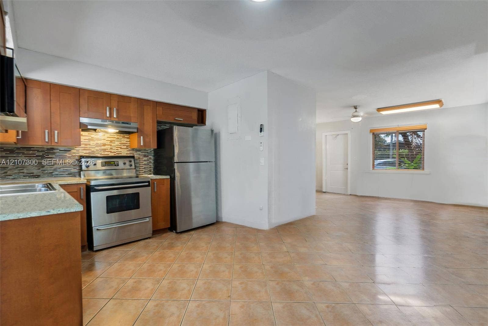 2051 NE 68th Street, Fort Lauderdale, FL 33308 Kitchen featuring natural wood cabinetry, stone-texture backsplash, stone-surface countertops, stainless steel appliances, and ceramic tile flooring