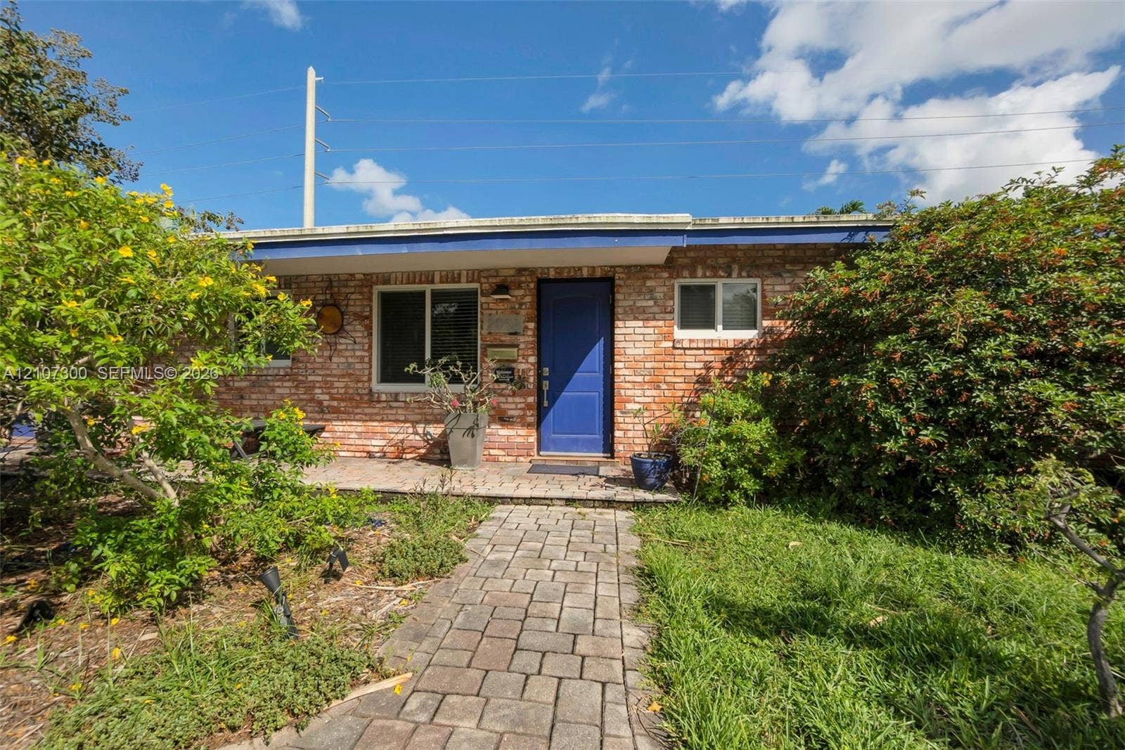 2051 NE 68th Street, Fort Lauderdale, FL 33308 Single-story brick exterior featuring a covered front porch, paver walkway, and blue entry door