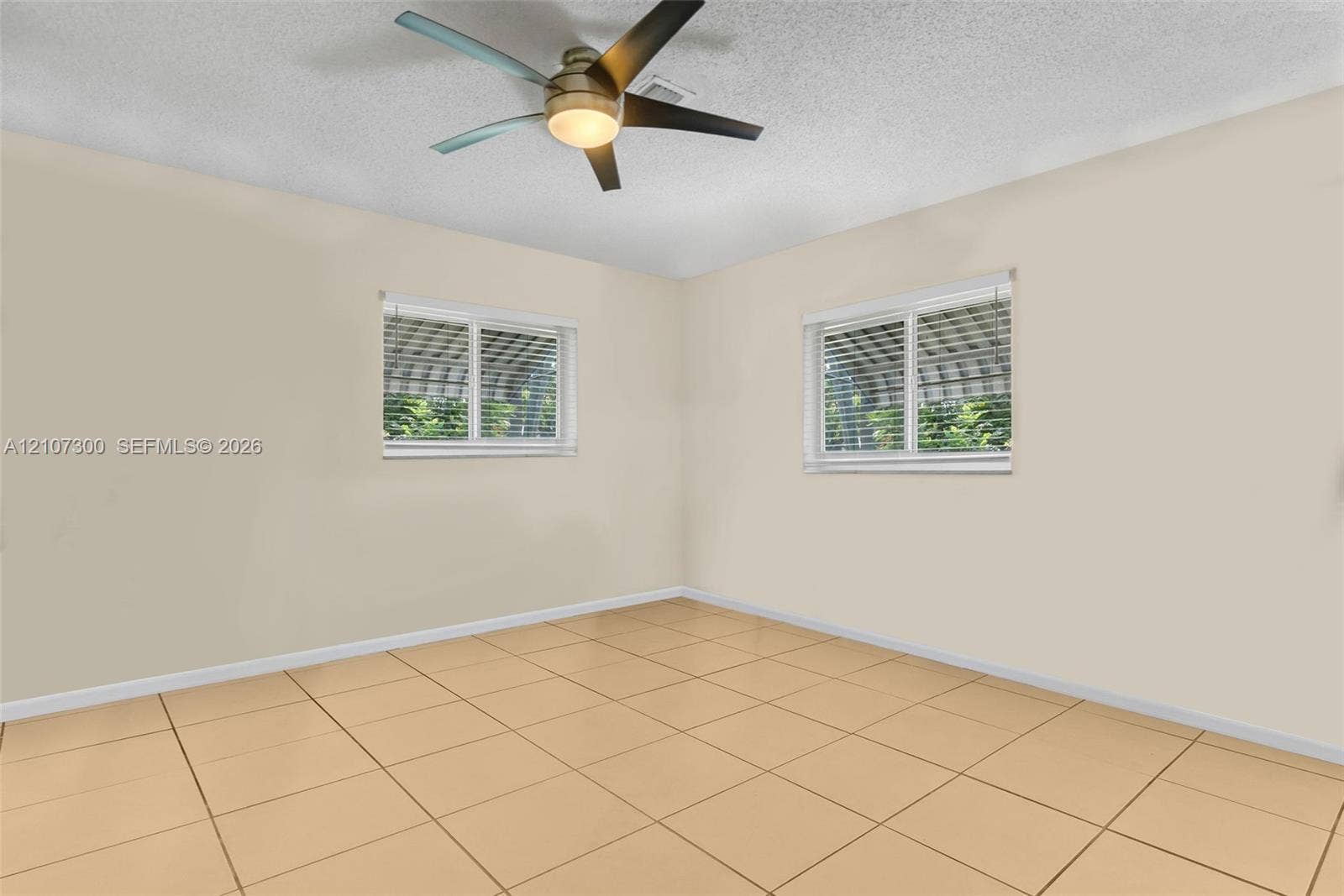 2051 NE 68th Street, Fort Lauderdale, FL 33308 Neutral interior featuring tile flooring, two windows with horizontal blinds, and a central ceiling fan with integrated lighting