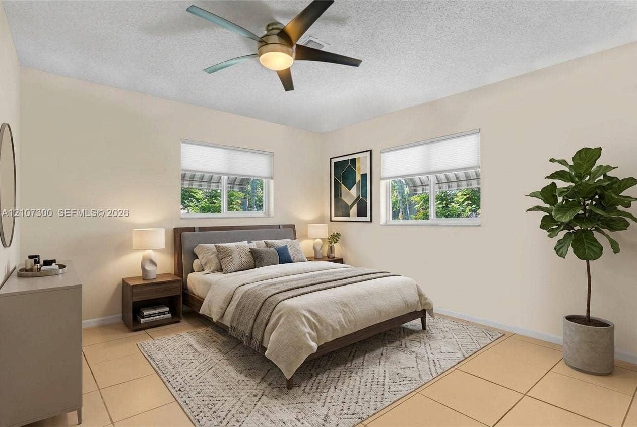 2051 NE 68th Street, Fort Lauderdale, FL 33308 Neutral-toned interior featuring large-format floor tiles, dual windows with fitted shades, and a ceiling fan with integrated lighting