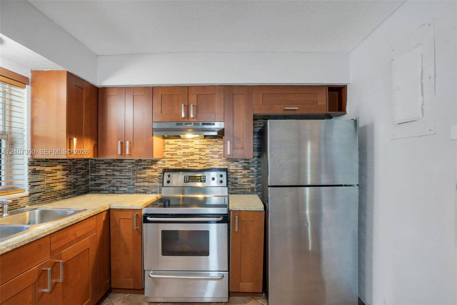 2051 NE 68th Street, Fort Lauderdale, FL 33308 Kitchen featuring warm-tone wood cabinetry, stone-finish countertops, stainless steel appliances, and a horizontal mosaic tile backsplash