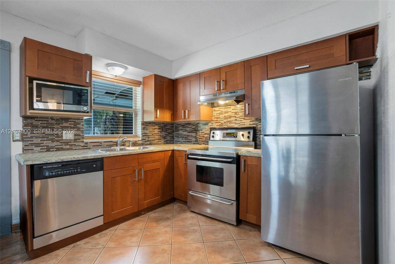 2051 NE 68th Street, Fort Lauderdale, FL 33308 Kitchen featuring wood cabinetry, stone-finish countertops, multi-toned horizontal tile backsplash, and stainless steel appliances including a range, microwave, and dishwasher