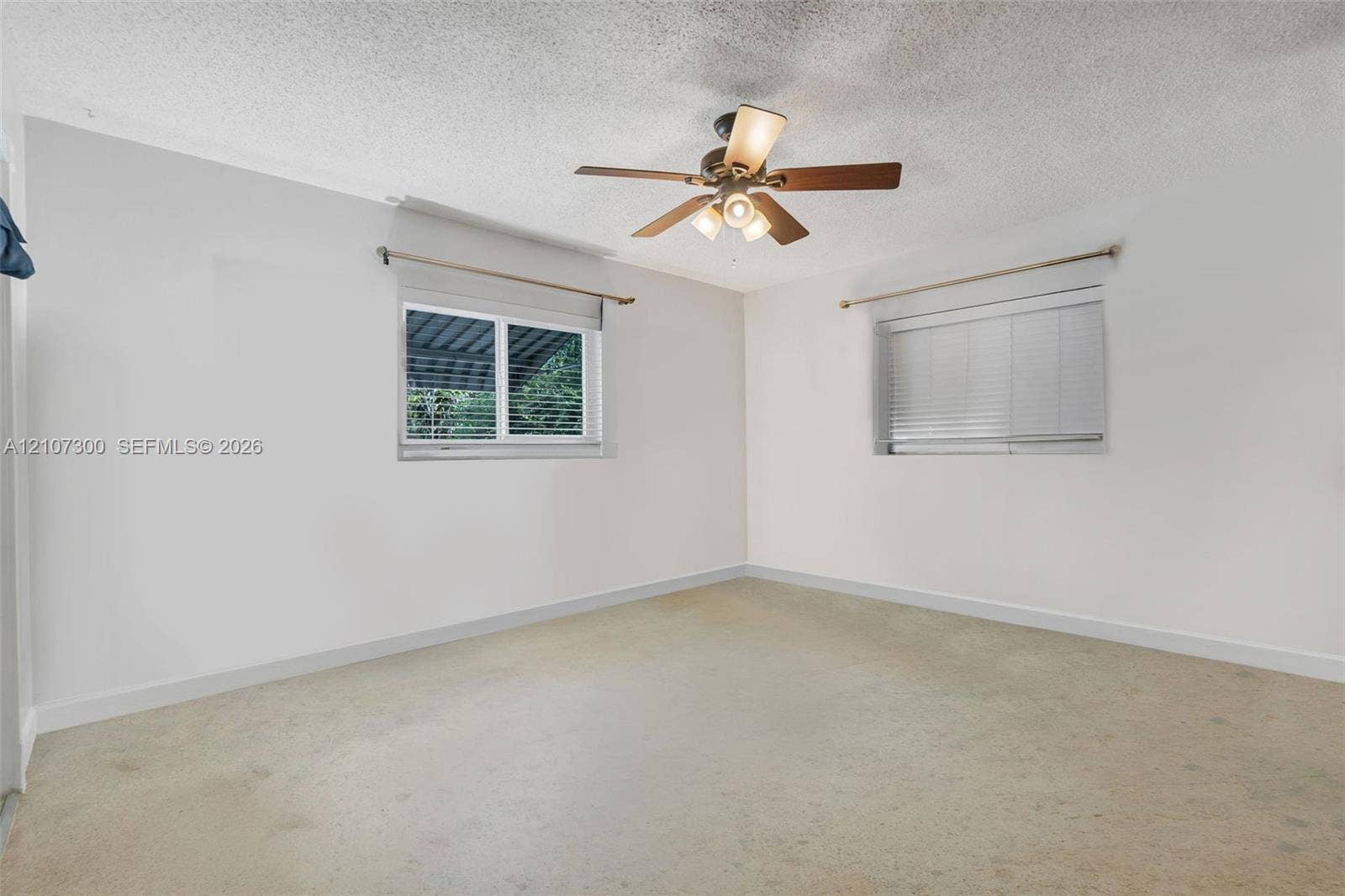 2051 NE 68th Street, Fort Lauderdale, FL 33308 Interior room featuring neutral wall finishes, carpeted flooring, two windows with horizontal blinds, and a ceiling fan with integrated lighting