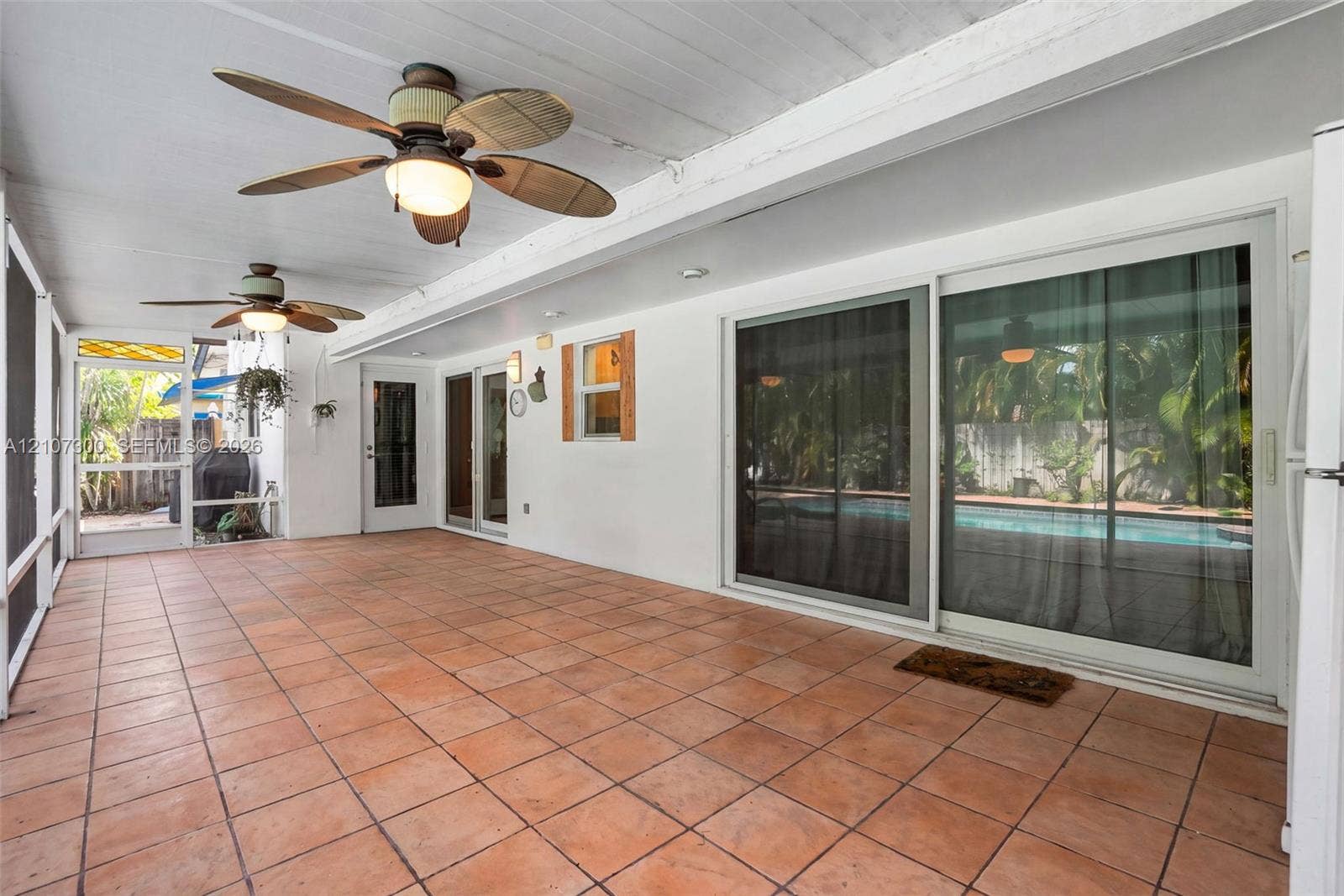 2051 NE 68th Street, Fort Lauderdale, FL 33308 Covered patio featuring terracotta tile flooring, two ceiling fans with integrated lighting, and multiple sliding glass door entries