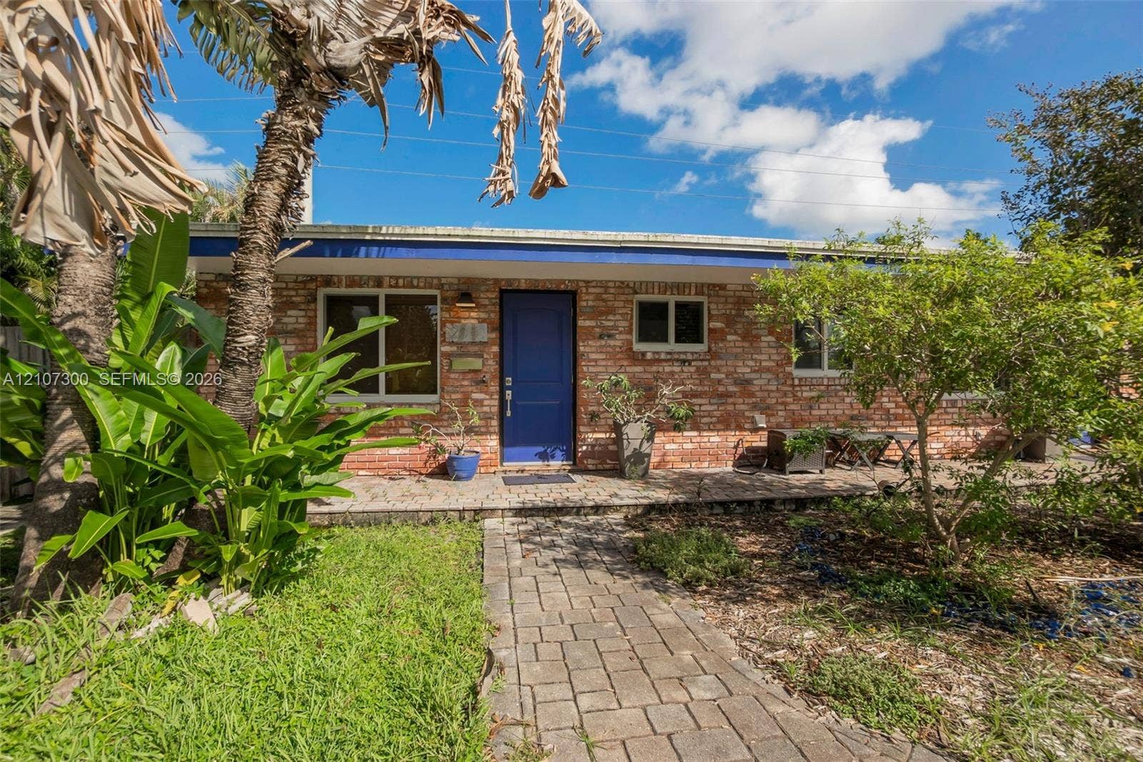 2051 NE 68th Street, Fort Lauderdale, FL 33308 Exterior elevation featuring a red brick facade, blue entry door, stone-paver walkway, and a flat roofline
