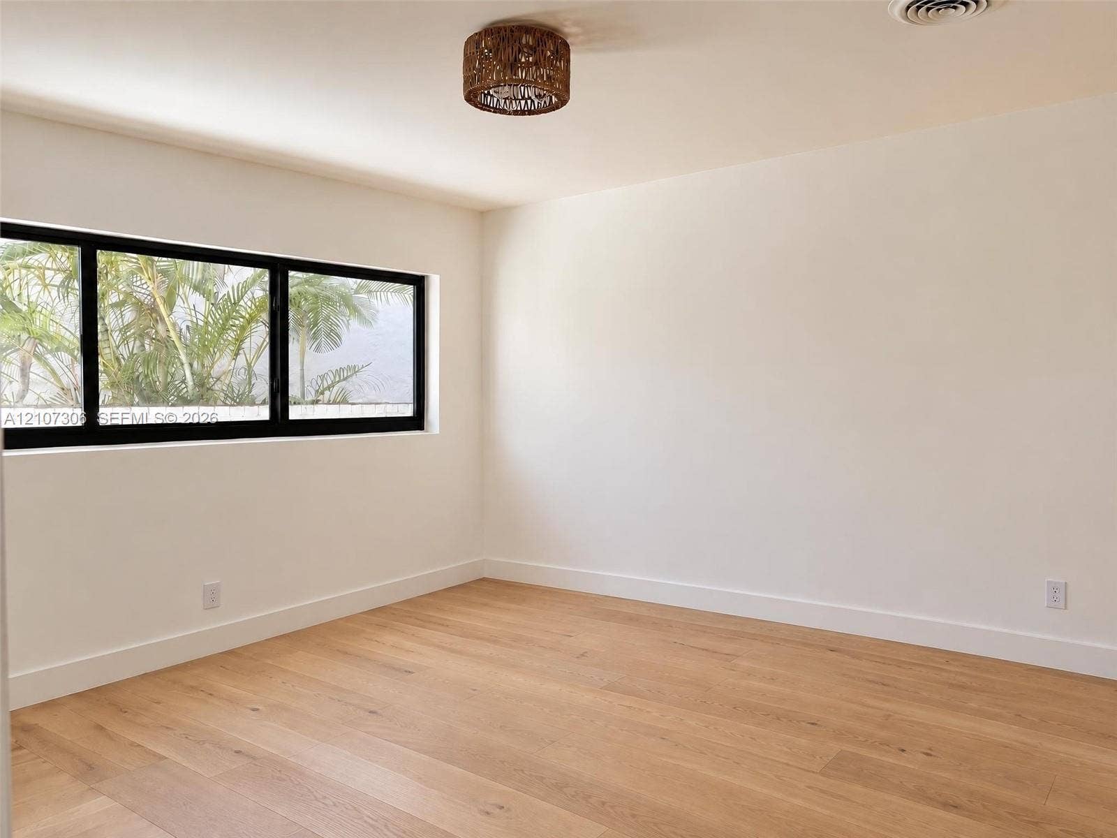 4322 Alton Road, Miami Beach, FL 33140 Neutral-toned interior featuring wood-finish flooring, a black-frame rectangular window, and a woven-textured flush-mount ceiling light