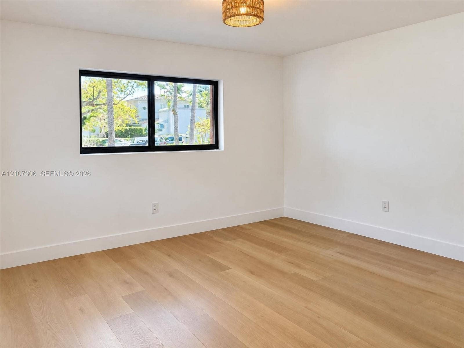4322 Alton Road, Miami Beach, FL 33140 Room featuring wood-finish flooring, white walls, black-framed horizontal window, and a woven drum light fixture