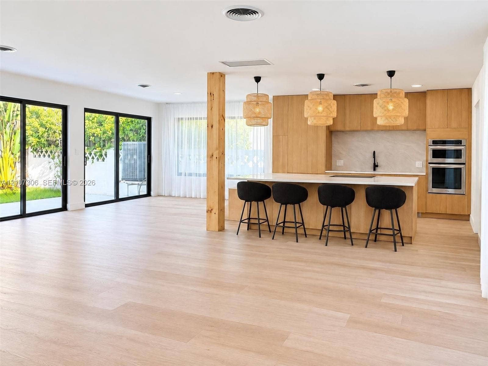 4322 Alton Road, Miami Beach, FL 33140 Kitchen featuring flat-panel wood cabinetry, a central island with a solid-surface countertop, built-in double ovens, wood-finish flooring, and dual sliding glass doors