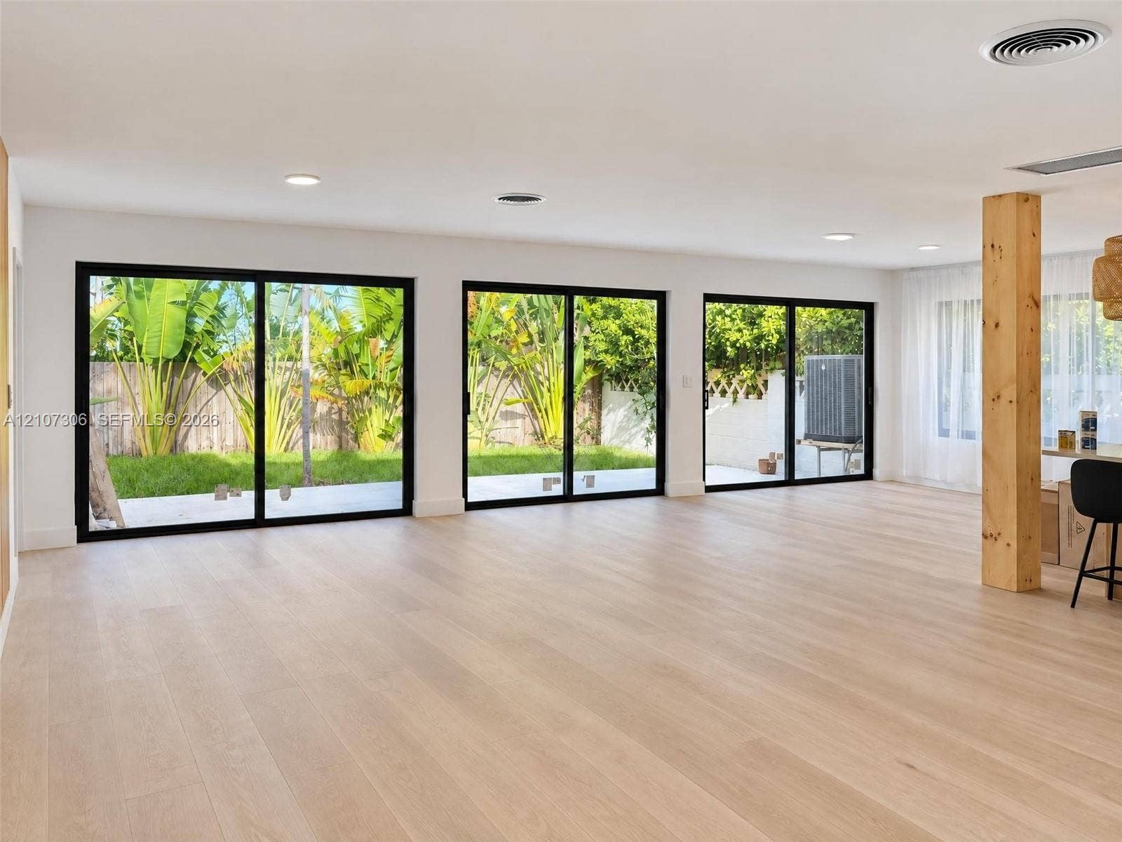 4322 Alton Road, Miami Beach, FL 33140 Interior space featuring three sets of black-framed sliding glass doors, light-toned wood-finish flooring, recessed ceiling lighting, and an exposed structural wood post