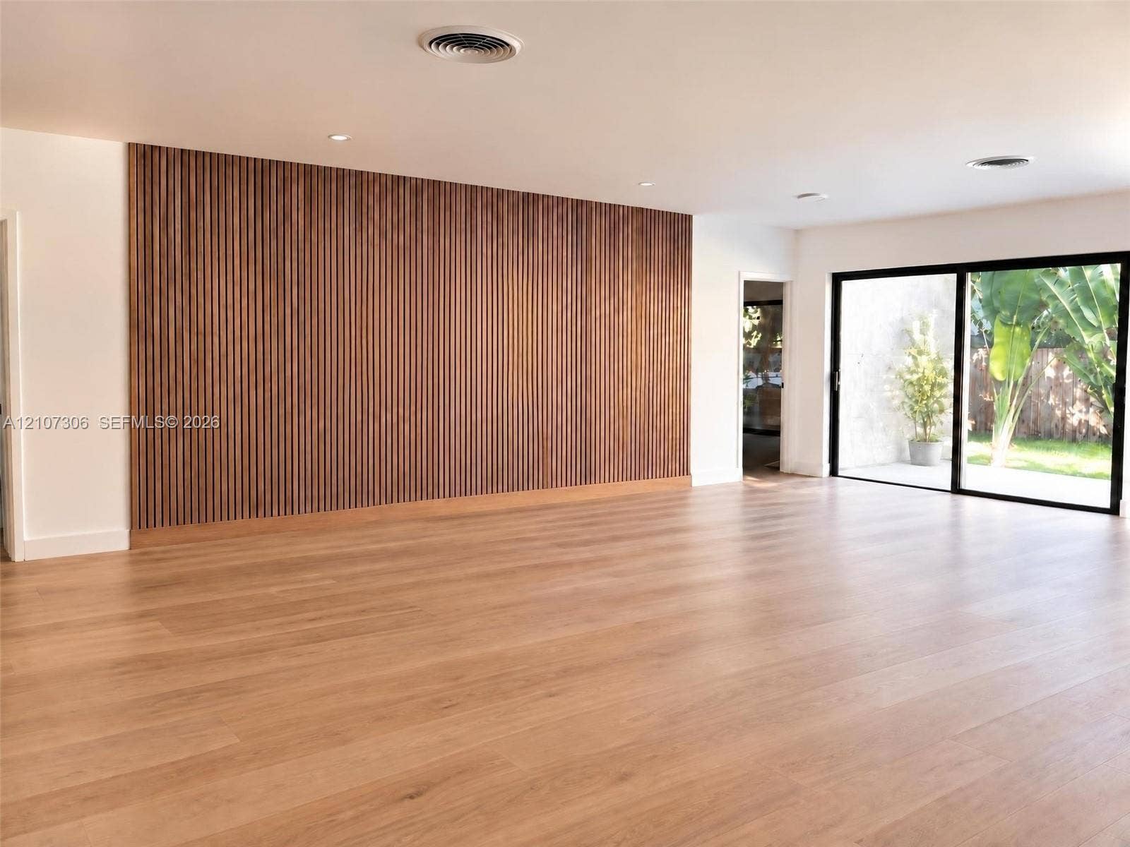 4322 Alton Road, Miami Beach, FL 33140 Expansive interior featuring wood-finish flooring, a floor-to-ceiling vertical wood slat accent wall, recessed lighting, and large sliding glass doors