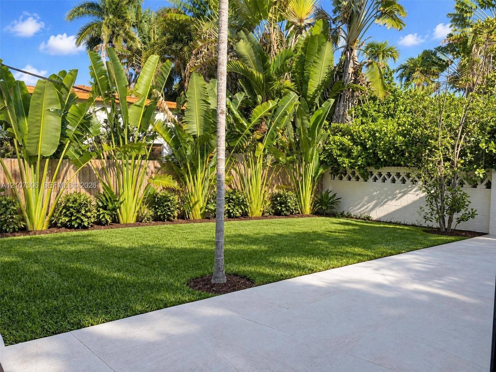 4322 Alton Road, Miami Beach, FL 33140 Private backyard featuring a paved stone patio, manicured lawn, established perimeter landscaping, and a decorative concrete masonry wall