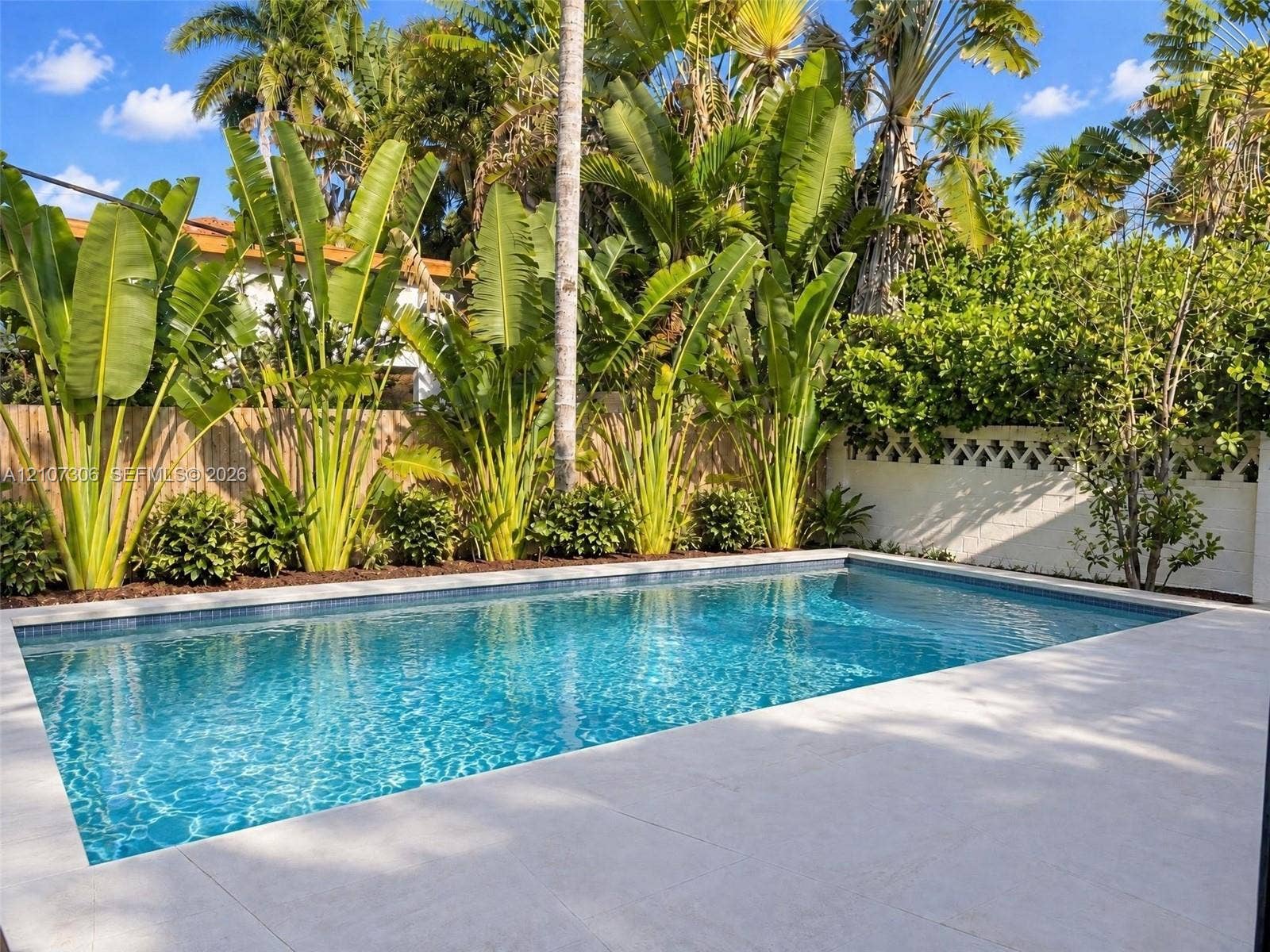 4322 Alton Road, Miami Beach, FL 33140 In-ground swimming pool with mosaic tile border, light-toned stone-finish patio, decorative masonry screen wall, and perimeter tropical landscaping