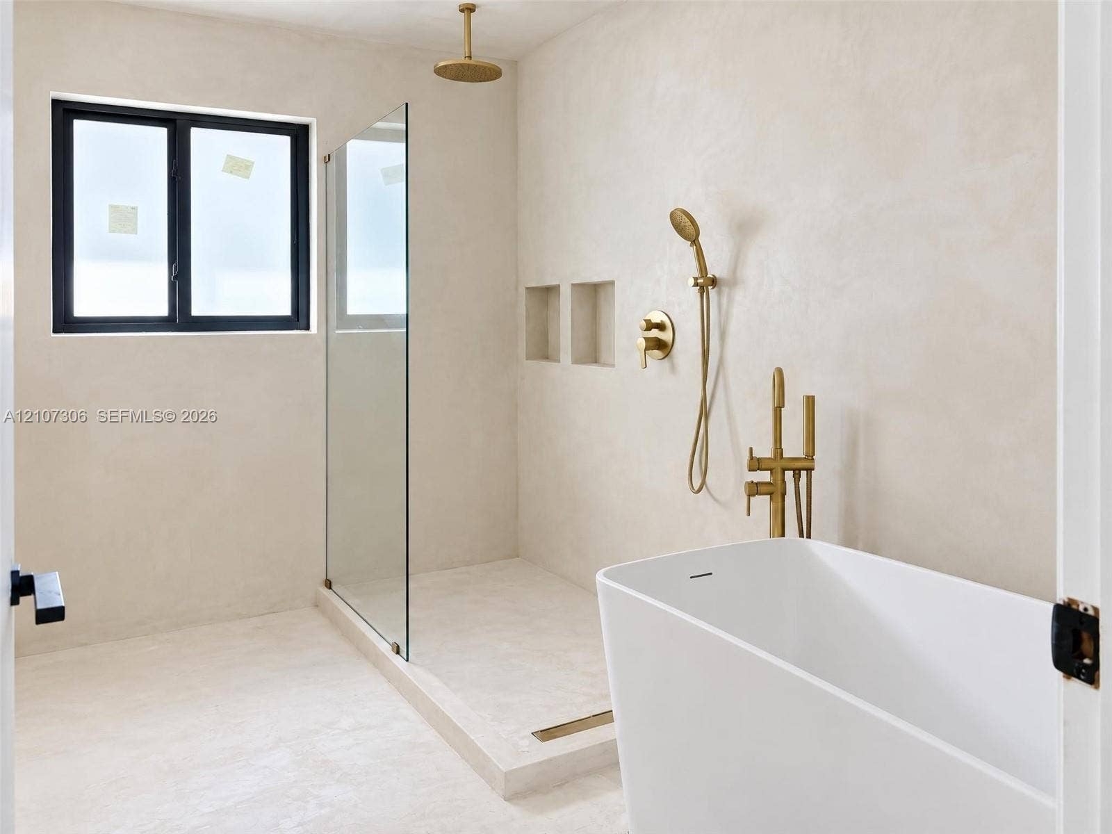 4322 Alton Road, Miami Beach, FL 33140 Freestanding soaking tub with brass fixtures, glass-enclosed walk-in shower, dual recessed wall niches, and matte-finish plaster wall treatment