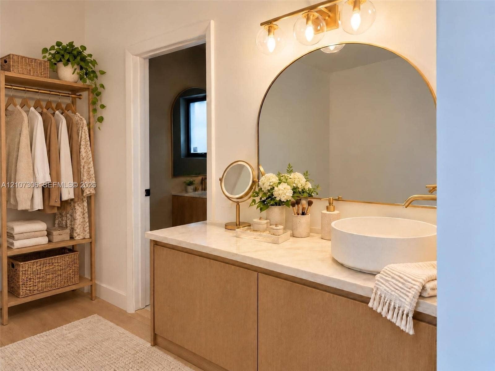 4322 Alton Road, Miami Beach, FL 33140 Custom wood-finish vanity with a neutral stone countertop, white vessel sink, arched wall mirror, and integrated gold-toned vanity lighting