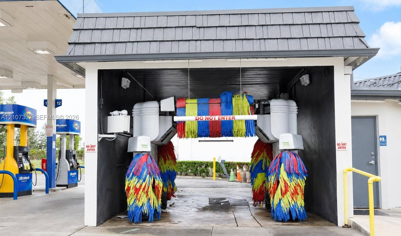 Automated car wash bay featuring an integrated brush system, overhead gabled roof structure, and concrete flooring