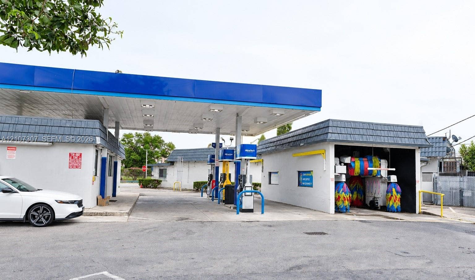 Commercial fuel station facility featuring a multi-pump canopy, integrated automated car wash bay, paved drive lanes, and masonry construction