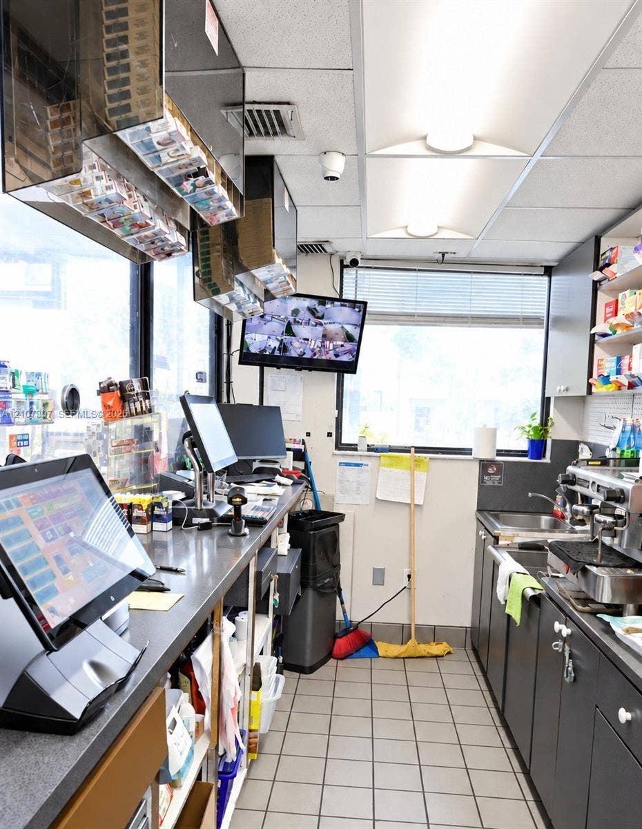 Service station workspace featuring industrial-grade metal counters, built-in dark cabinetry, a multi-basin stainless steel sink, and light-tone ceramic floor tiling