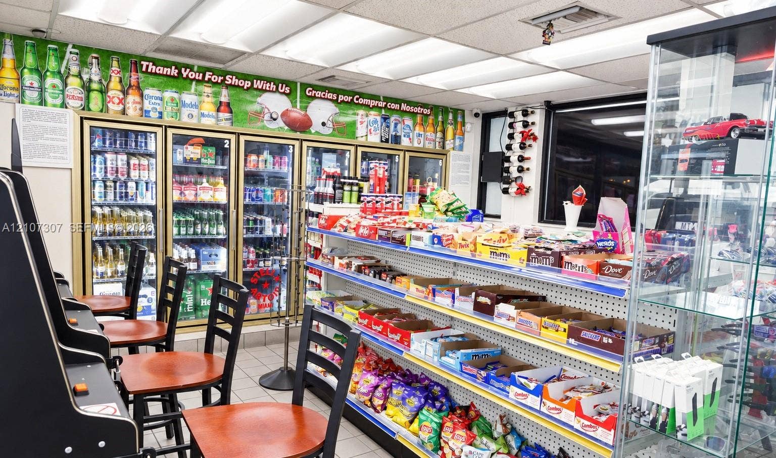 Commercial retail space featuring multi-door glass-front refrigerated display cases, wall-mounted wine rack, built-in pegboard shelving units, and a glass display cabinet
