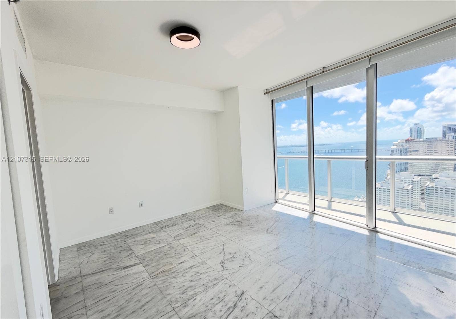 495 Brickell Avenue, #3803, Miami, FL 33131 Floor-to-ceiling sliding glass doors, polished stone tile flooring, circular flush-mount ceiling lighting, and private balcony with water and skyline backdrop