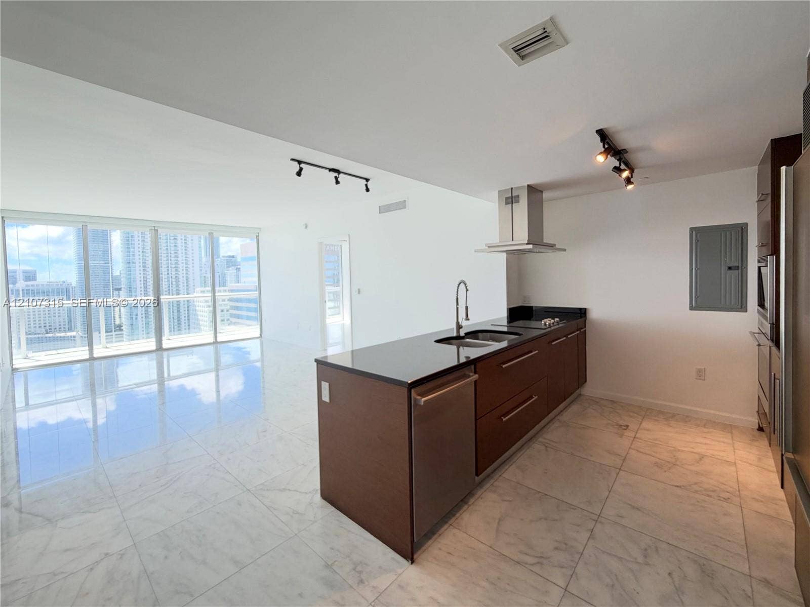 495 Brickell Avenue, #3803, Miami, FL 33131 Kitchen featuring dark wood-finish cabinetry, stone countertops, stainless steel appliances, and a stainless steel chimney-style range hood, complemented by large-format light-toned flooring and floor-to-ceiling glass panel windows