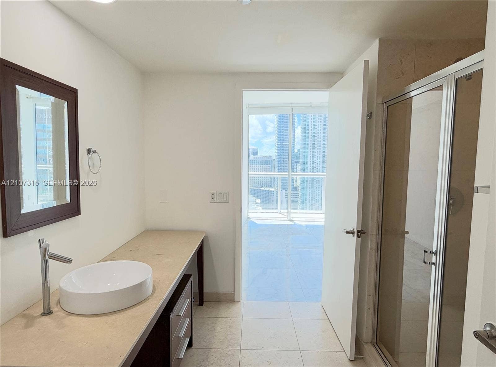 495 Brickell Avenue, #3803, Miami, FL 33131 Bathroom featuring a vanity with a stone countertop, a white vessel sink, a wall-mounted framed mirror, and a glass-enclosed shower