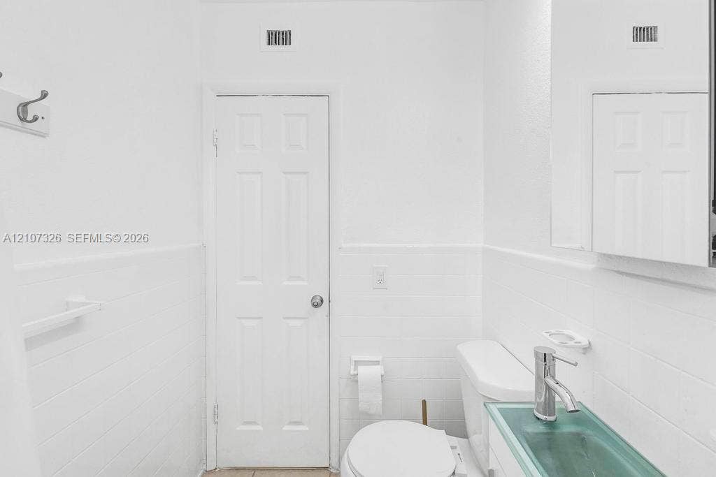 1801 NE 154th Street, #0, North Miami Beach, North Miami Beach, FL 33162 White subway tile wall cladding, single-panel interior door, medicine cabinet with mirrored front, and glass vessel sink with chrome-finish faucet