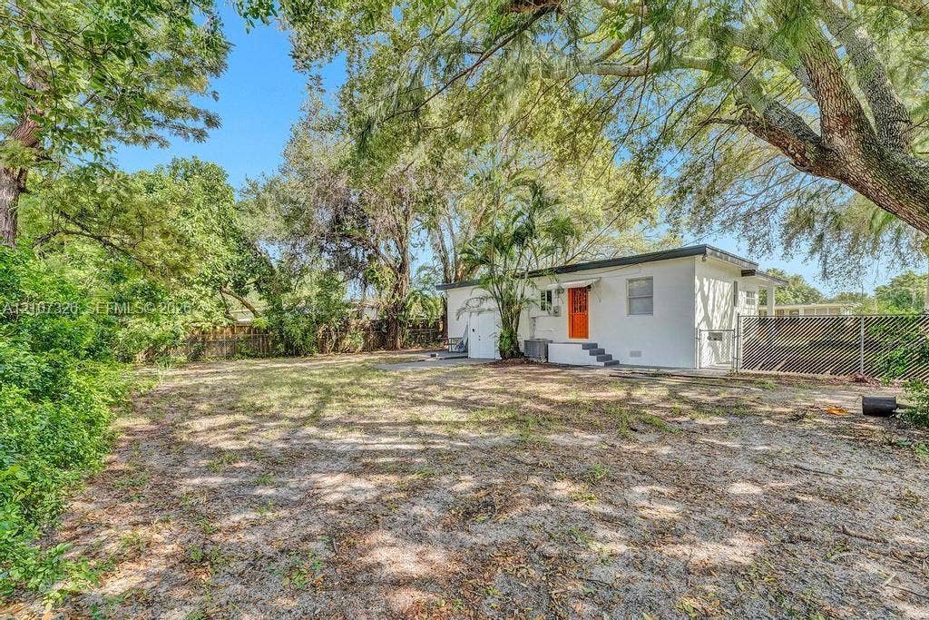 1801 NE 154th Street, #0, North Miami Beach, North Miami Beach, FL 33162 Expansive backyard featuring mature shade trees, chain-link perimeter fencing, and a white stucco exterior structure with a prominent orange entry door