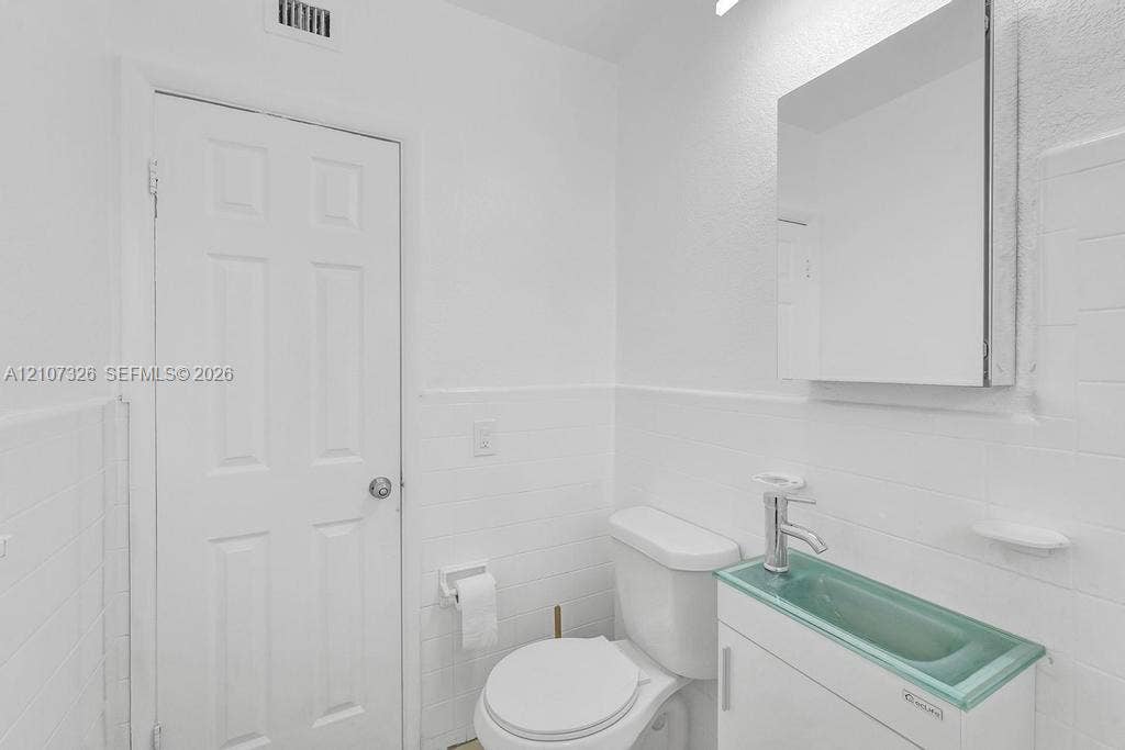 1801 NE 154th Street, #0, North Miami Beach, North Miami Beach, FL 33162 Bathroom featuring white tile wall cladding, a floating vanity with a glass basin and integrated faucet, and a wall-mounted mirrored medicine cabinet
