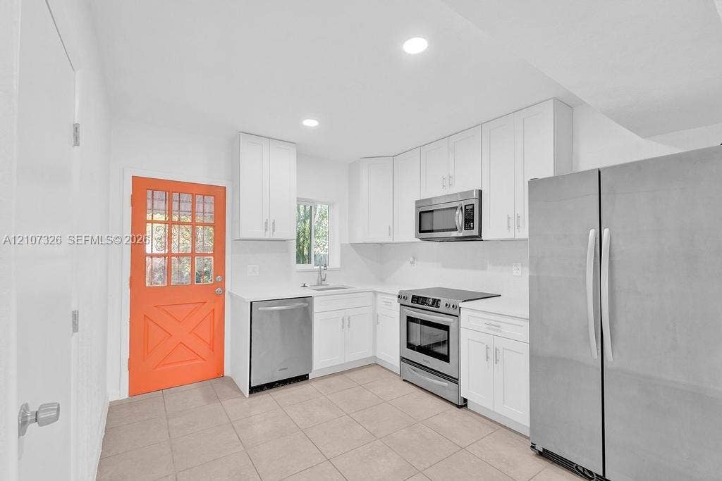 1801 NE 154th Street, #0, North Miami Beach, North Miami Beach, FL 33162 Kitchen featuring white shaker-style cabinetry, solid-surface countertops, stainless steel appliances, tile flooring, and a glass-paneled exterior door