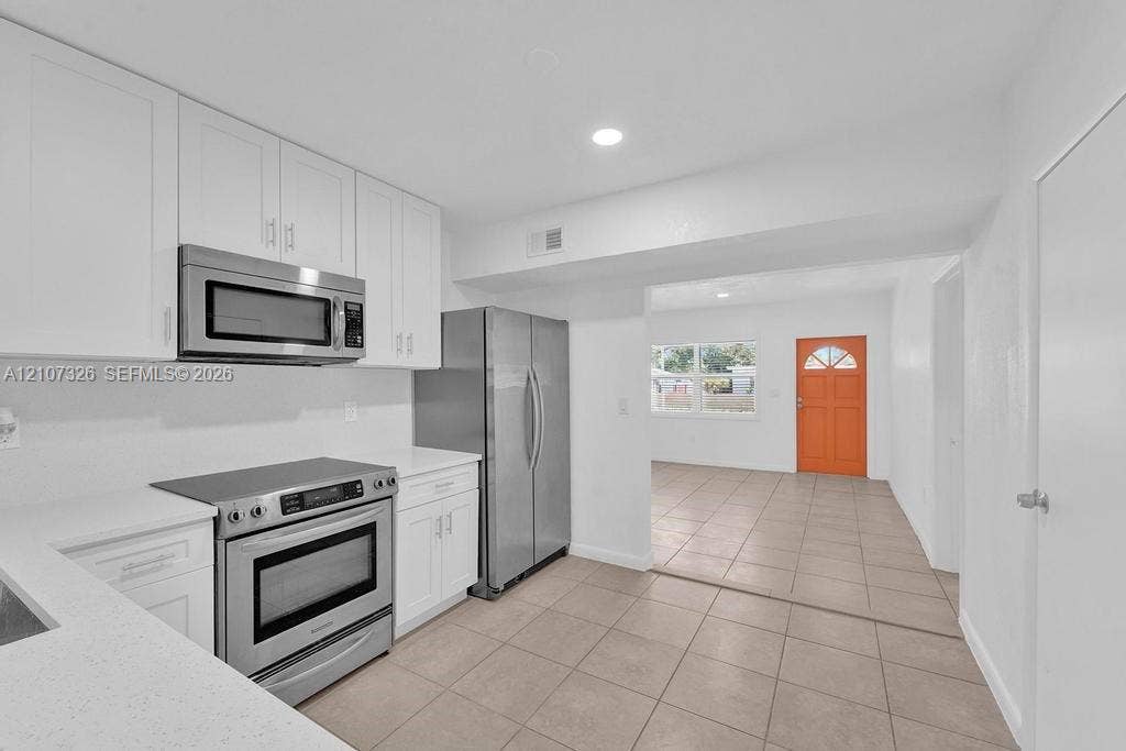 1801 NE 154th Street, #0, North Miami Beach, North Miami Beach, FL 33162 Kitchen featuring white cabinetry, solid-surface countertops, and stainless steel appliances including a built-in microwave, range, and refrigerator