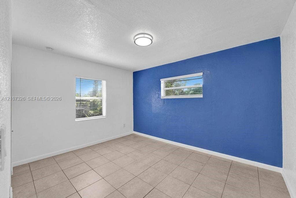 1801 NE 154th Street, #0, North Miami Beach, North Miami Beach, FL 33162 Interior room featuring neutral ceramic tile flooring, a prominent accent wall, two windows with horizontal blinds, and a flush-mount ceiling light fixture