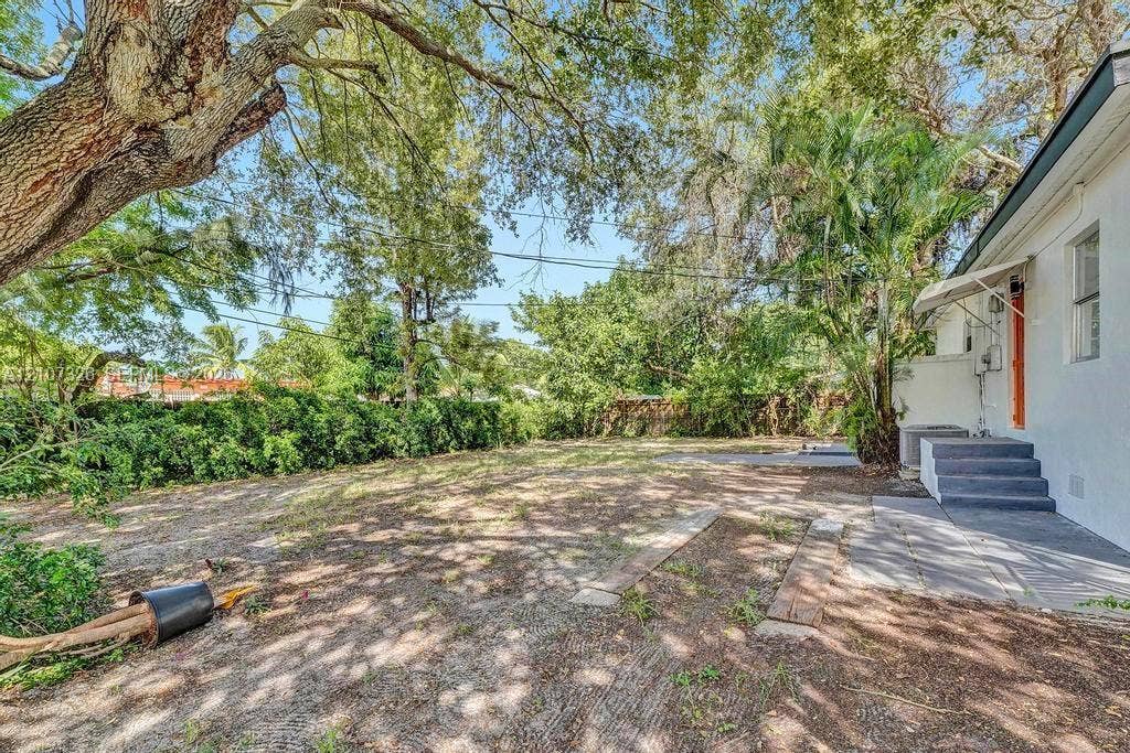 1801 NE 154th Street, #0, North Miami Beach, North Miami Beach, FL 33162 Backyard space featuring mature shade trees, established perimeter shrubbery, concrete patio area, and elevated concrete steps with a metal awning