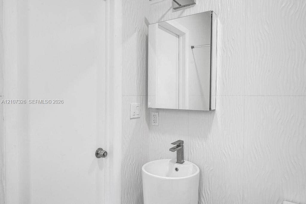 1801 NE 154th Street, #0, North Miami Beach, North Miami Beach, FL 33162 Wall-mounted medicine cabinet with a mirror, cylindrical pedestal sink, single-lever faucet, and textured tile wall cladding