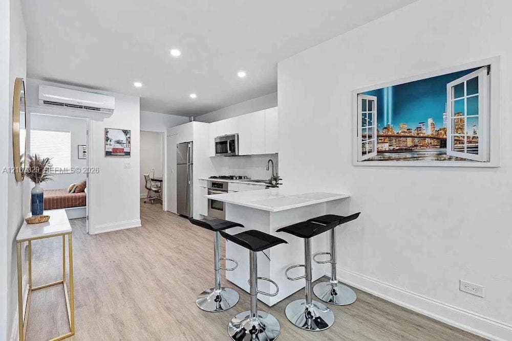 830 9th Street, #14, Miami Beach, Miami Beach, FL 33139 Kitchen featuring white flat-panel cabinetry, stainless steel appliances, a peninsula with stone-finish countertop, wood-finish flooring, and recessed lighting