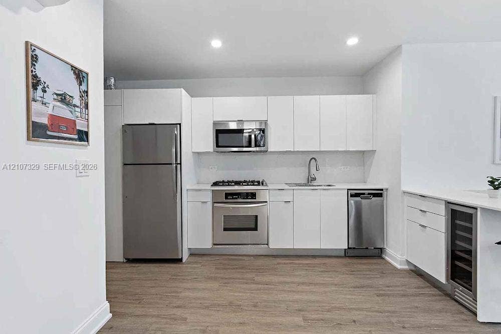 830 9th Street, #14, Miami Beach, Miami Beach, FL 33139 Kitchen featuring white flat-panel cabinetry, stainless steel appliances, a gas cooktop, quartz countertops, and an under-counter beverage refrigerator, set over wood-finish flooring