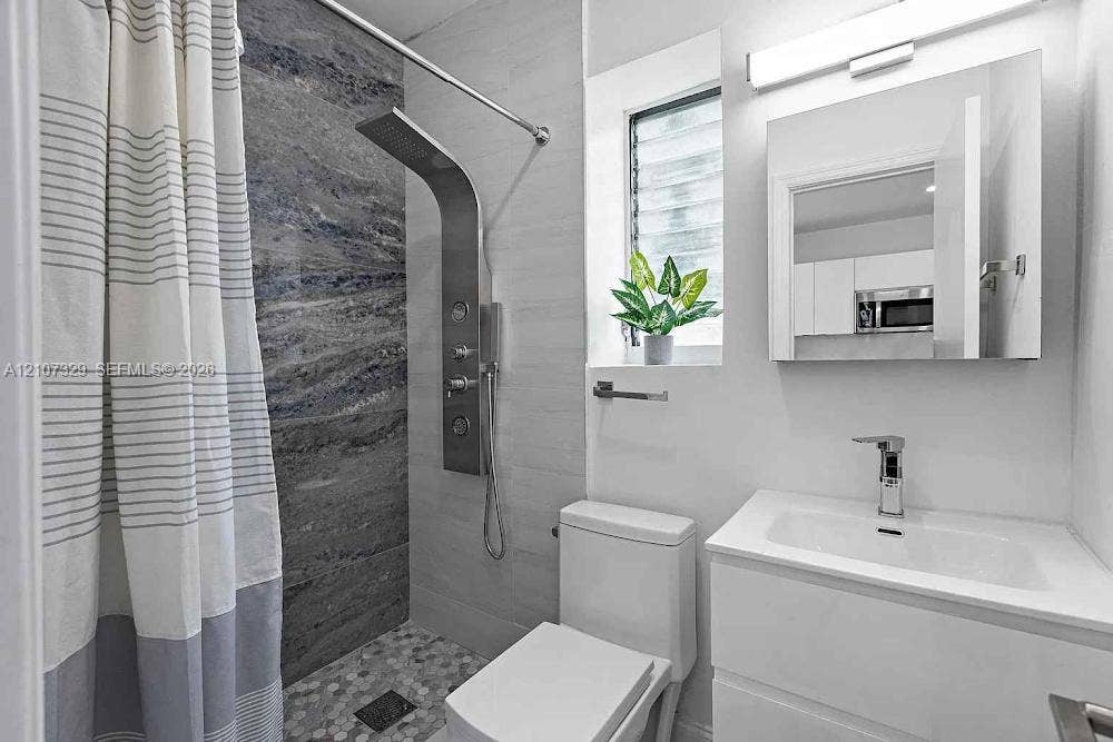 830 9th Street, #14, Miami Beach, Miami Beach, FL 33139 Shower stall featuring a multi-function stainless steel panel system and textured stone-finish tile surround with pebble-style floor tiling, complemented by a modern white vanity with integrated sink and mirrored medicine cabinet