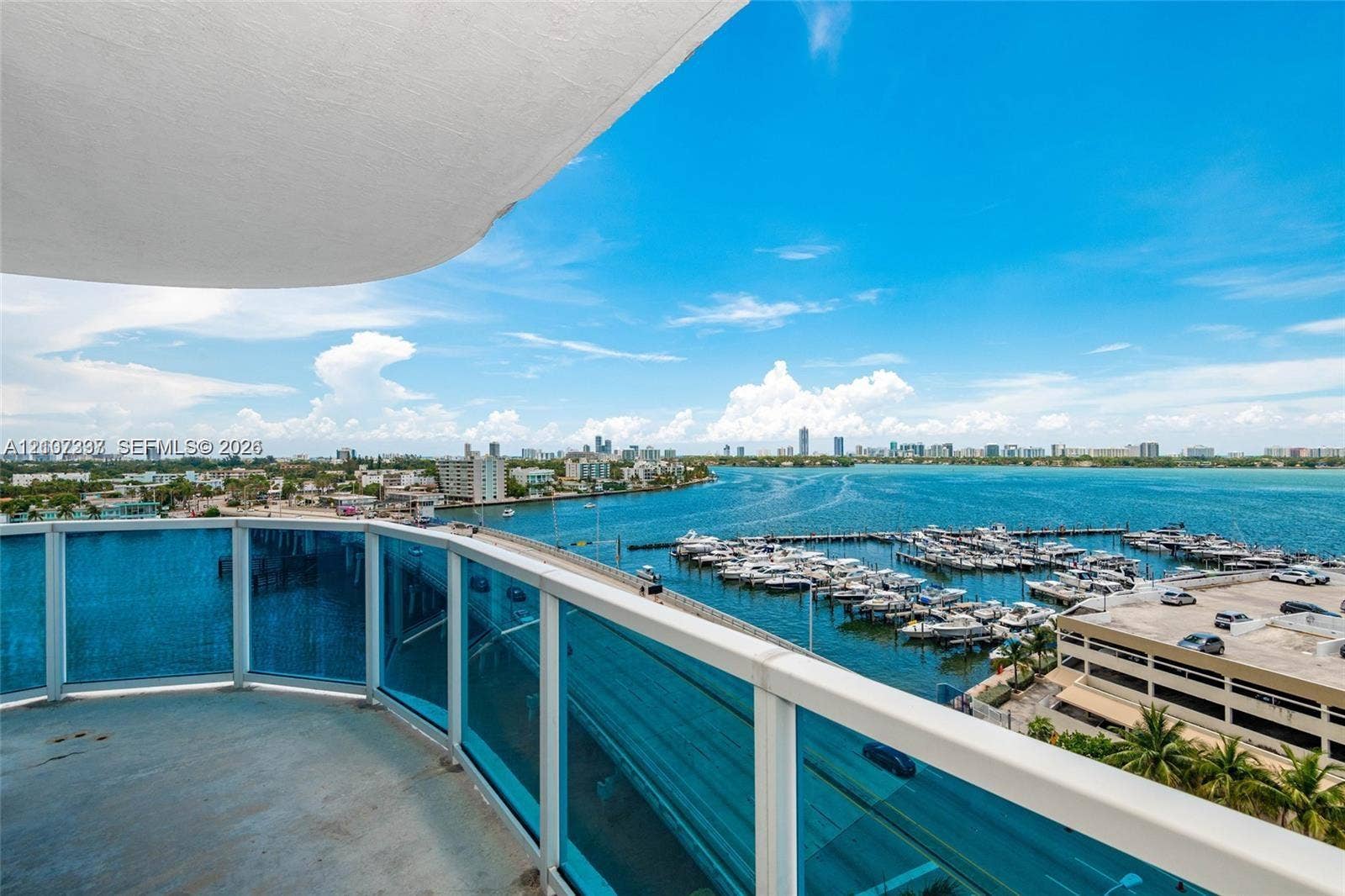 1881 79th St Causeway, #1007, North Bay Village, FL 33141 Private balcony featuring blue-tinted glass railings and concrete flooring, overlooking an expansive marina, open water, and coastal horizon