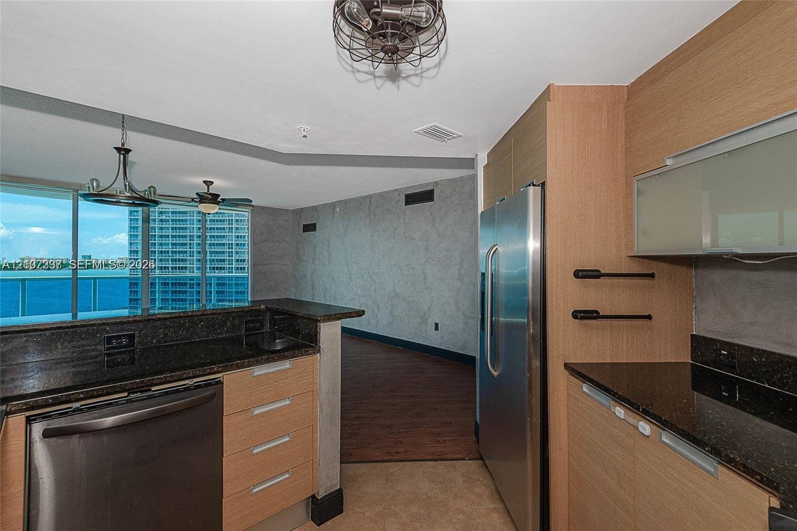 1881 79th St Causeway, #1007, North Bay Village, FL 33141 Kitchen featuring flat-panel wood cabinetry, dark stone countertops, stainless steel refrigerator, and industrial-style cage lighting