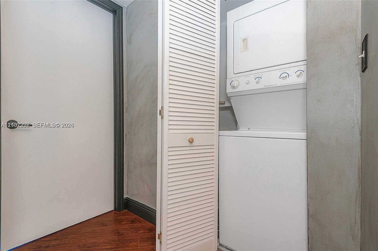 1881 79th St Causeway, #1007, North Bay Village, FL 33141 Laundry closet featuring a white stacked washer and dryer unit, louvered bi-fold door, dark trim accents, and wood-finish flooring