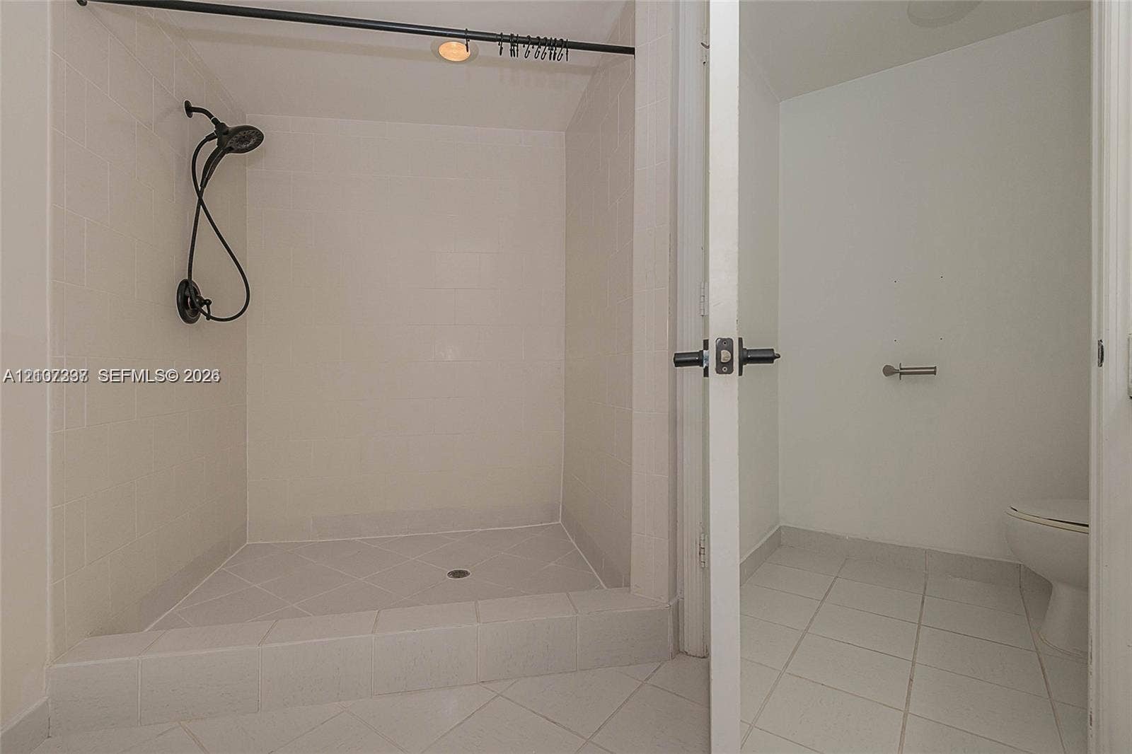 1881 79th St Causeway, #1007, North Bay Village, FL 33141 Walk-in shower featuring white tiled walls, a matte black handheld showerhead, a raised threshold, and white floor tile throughout