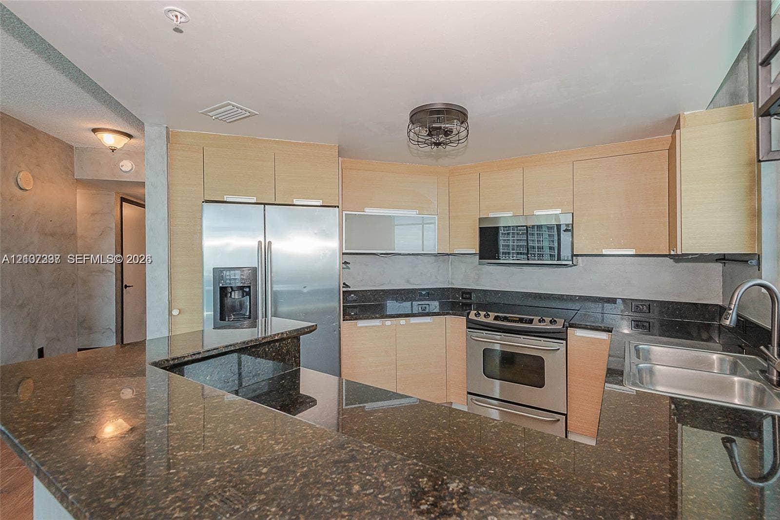 1881 79th St Causeway, #1007, North Bay Village, FL 33141 Kitchen featuring flat-panel light wood cabinetry, dark stone countertops, stainless steel appliances, breakfast bar, and stainless steel dual-basin sink