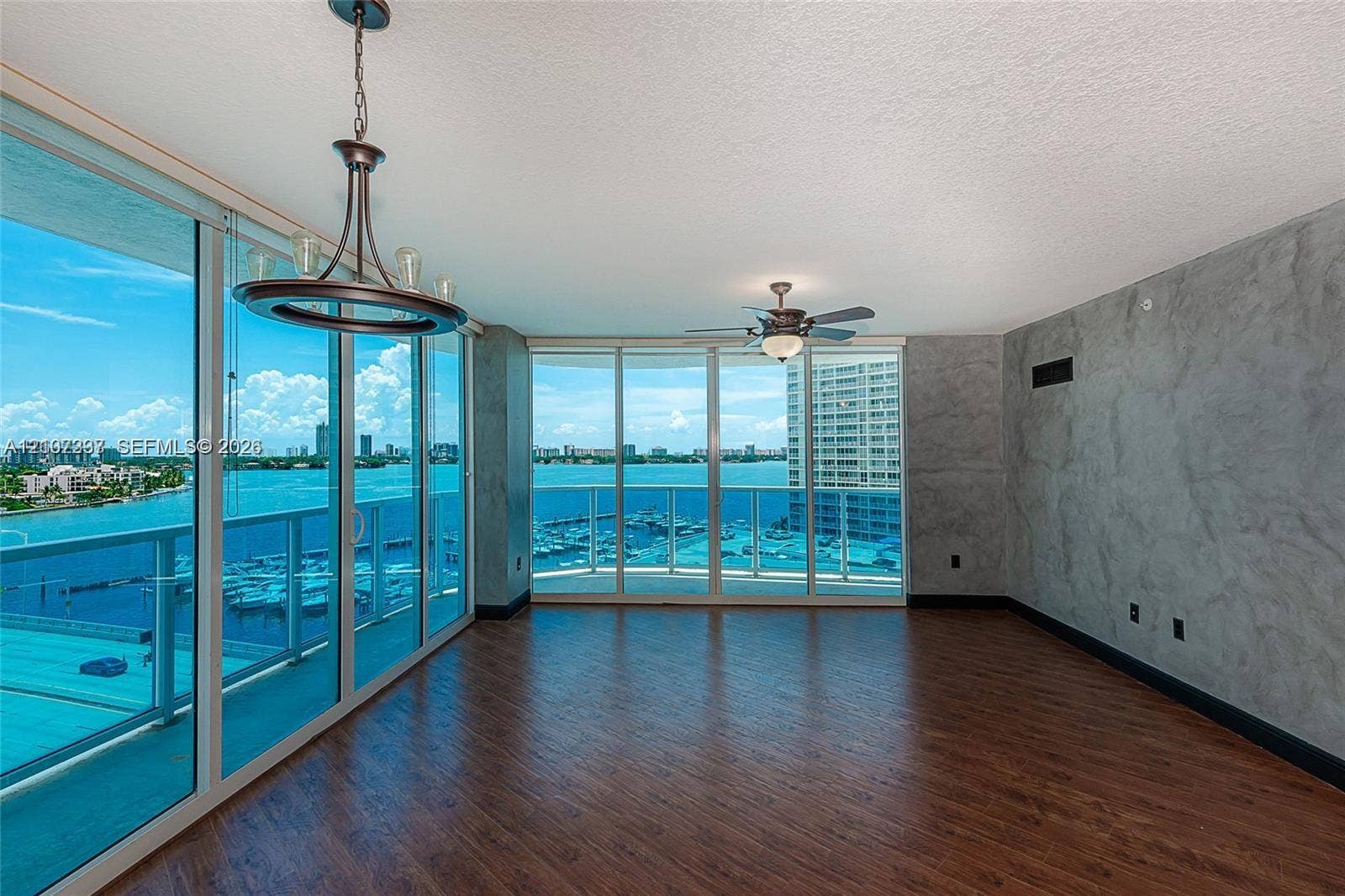 1881 79th St Causeway, #1007, North Bay Village, FL 33141 Floor-to-ceiling glass windows, wood-finish flooring, custom textured wall finish, integrated ceiling fan, and multi-light chandelier