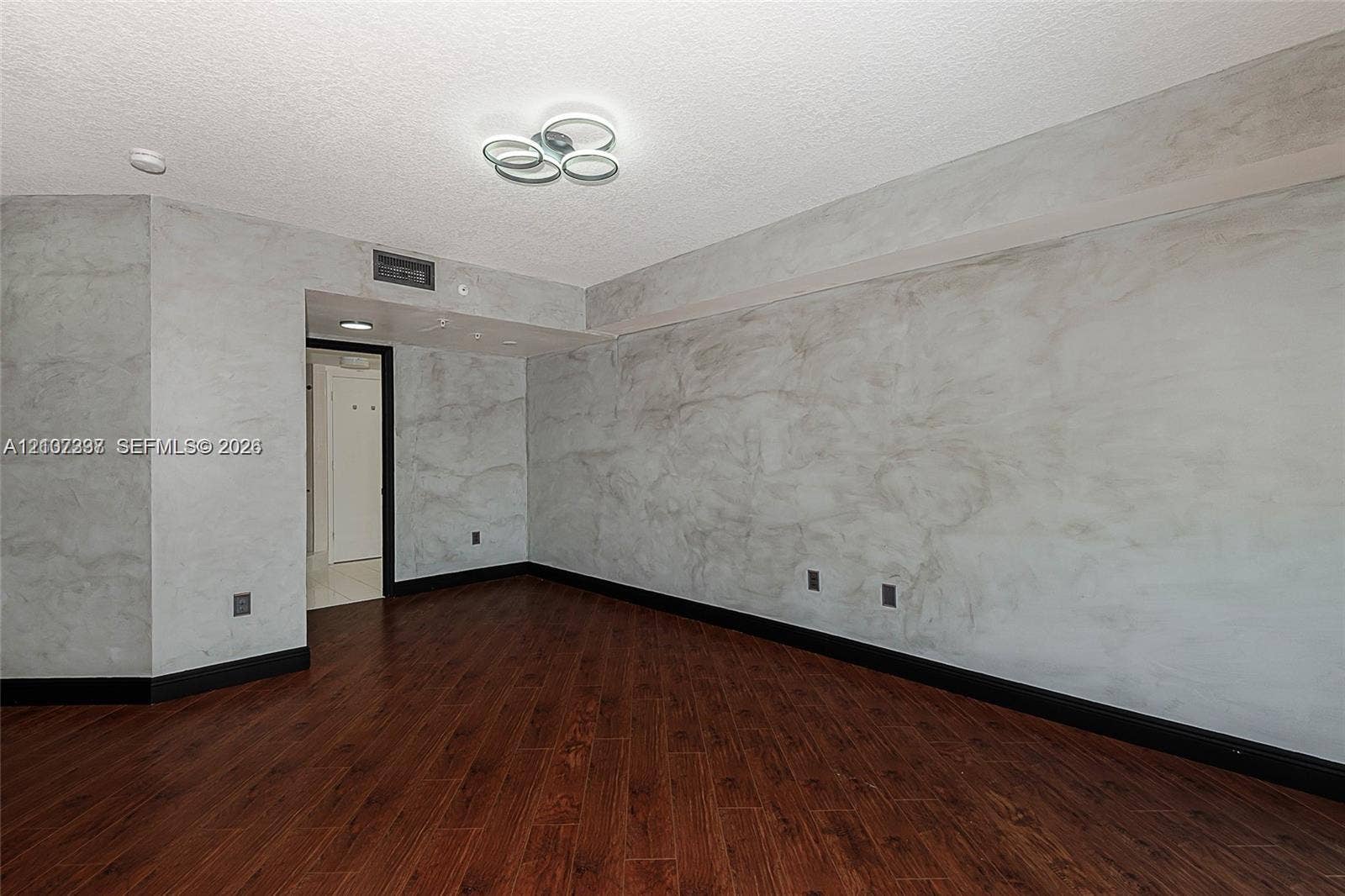 1881 79th St Causeway, #1007, North Bay Village, FL 33141 Interior room featuring wood-finish flooring, decorative marble-patterned wall finishes, and a modern circular multi-ring flush-mount light fixture