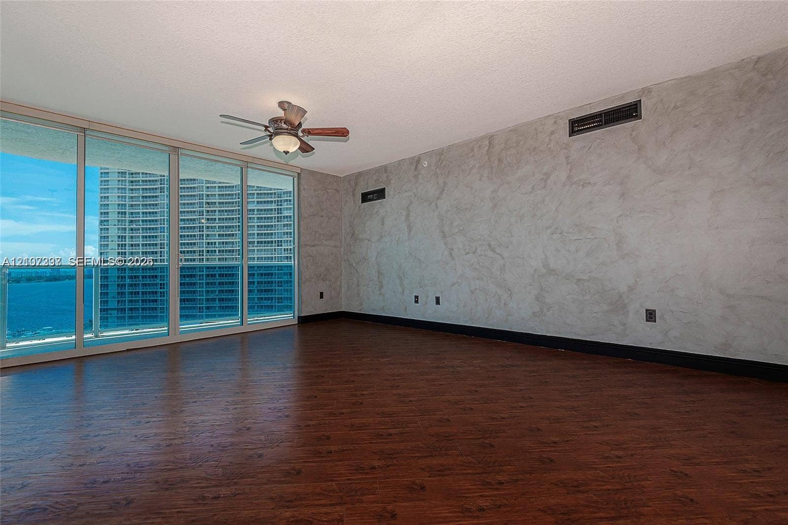 1881 79th St Causeway, #1007, North Bay Village, FL 33141 Floor-to-ceiling sliding glass doors, dark wood-finish flooring, decorative plaster wall finish, and a ceiling-mounted lighting fixture with an integrated fan