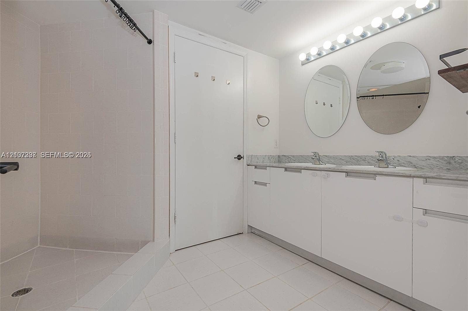 1881 79th St Causeway, #1007, North Bay Village, FL 33141 Bathroom featuring a dual-sink vanity with stone countertop, twin circular mirrors, a multi-bulb light fixture, and a walk-in shower with tile surround