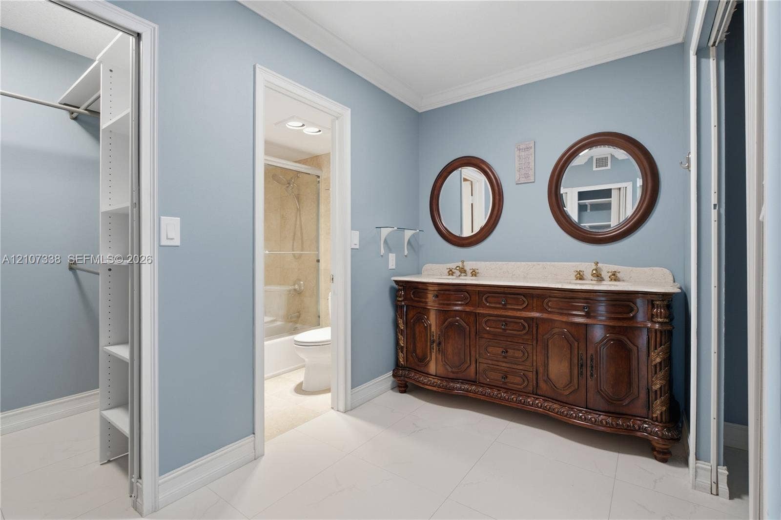 20355 NE 34th Court, #1824, Aventura, FL 33180 Double vanity featuring wood cabinetry, stone-surface countertop, dual round mirrors, and built-in closet shelving