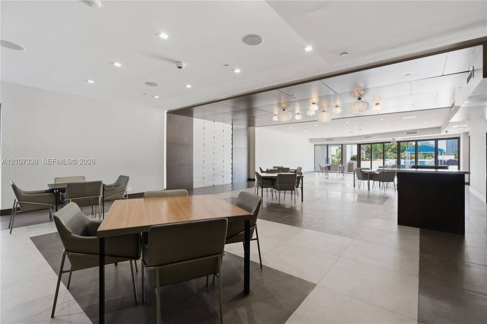 20355 NE 34th Court, #1824, Aventura, FL 33180 Spacious interior featuring large-format tile flooring, a dark-toned drop ceiling with integrated recessed lighting, decorative globe pendant lights, and floor-to-ceiling glass panel doors