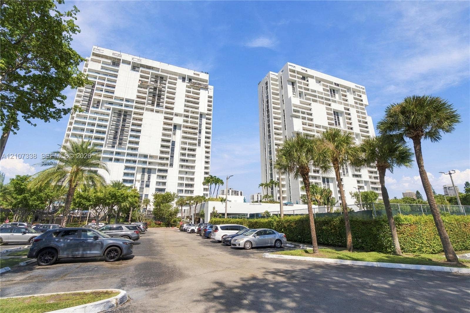 20355 NE 34th Court, #1824, Aventura, FL 33180 High-rise residential towers featuring white concrete facades, multiple levels of private balconies, and an extensive parking area with mature palm trees
