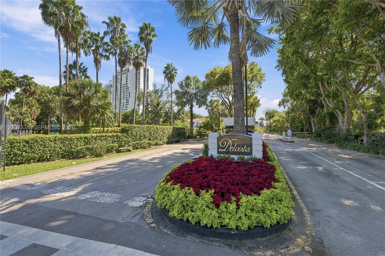 20355 NE 34th Court, #1824, Aventura, FL 33180 Community entrance featuring a monument sign, landscaped island with decorative plantings, palm trees, and mature canopy trees